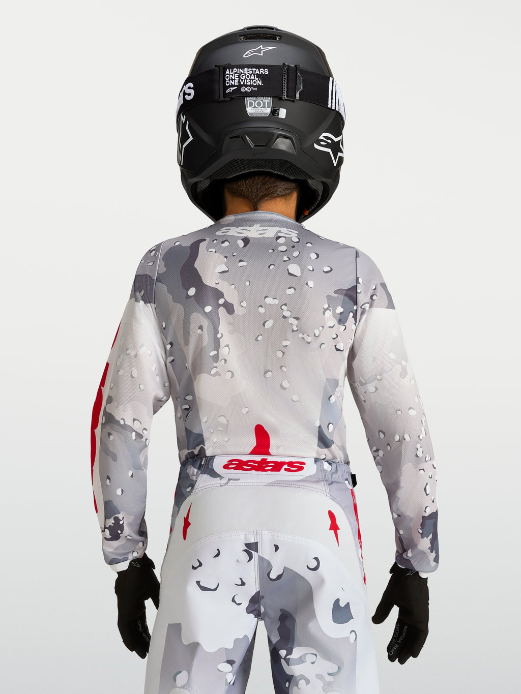 Alpinestars Maglia Fluid Lone Ragazzo 2027, maglia da motocross grigio camouflage, vista posteriore con dettagli rossi e casco nero, abbigliamento off-road per giovani piloti