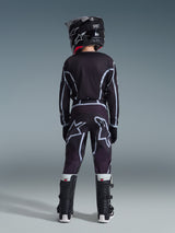 Giovane pilota di motocross visto da dietro che indossa la maglia Alpinestars Youth Fluid Apex 2026 in nero e grigio, pantaloni coordinati con grandi loghi bianchi, casco nero e stivali Tech Series bianchi e neri, set completo per il fuoristrada.