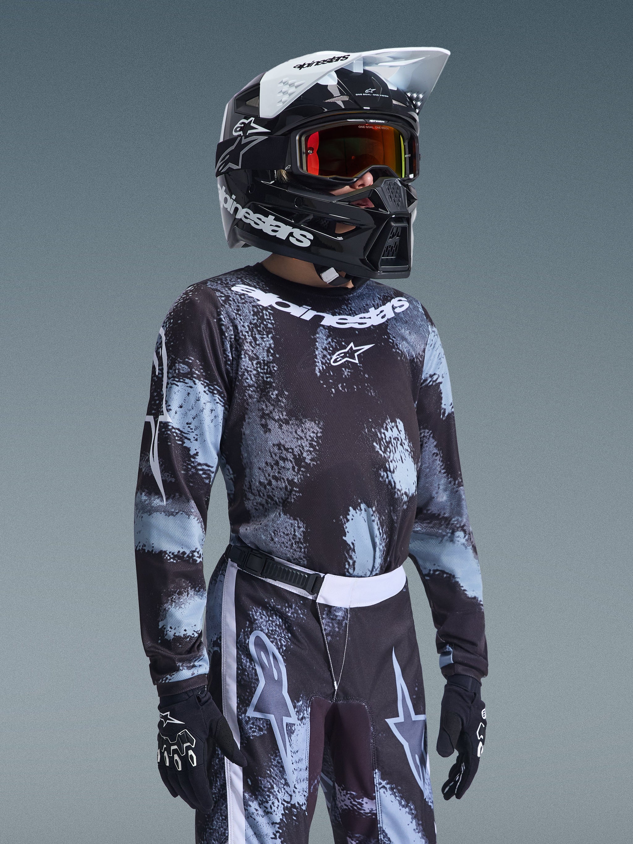 Maglia Alpinestars Youth Fluid Lahnd 2026, maglia da motocross, pattern Iron Camo in nero e azzurro, indossata da un giovane pilota con pantaloni coordinati e casco nero, equipaggiamento da gara fuoristrada coordinato