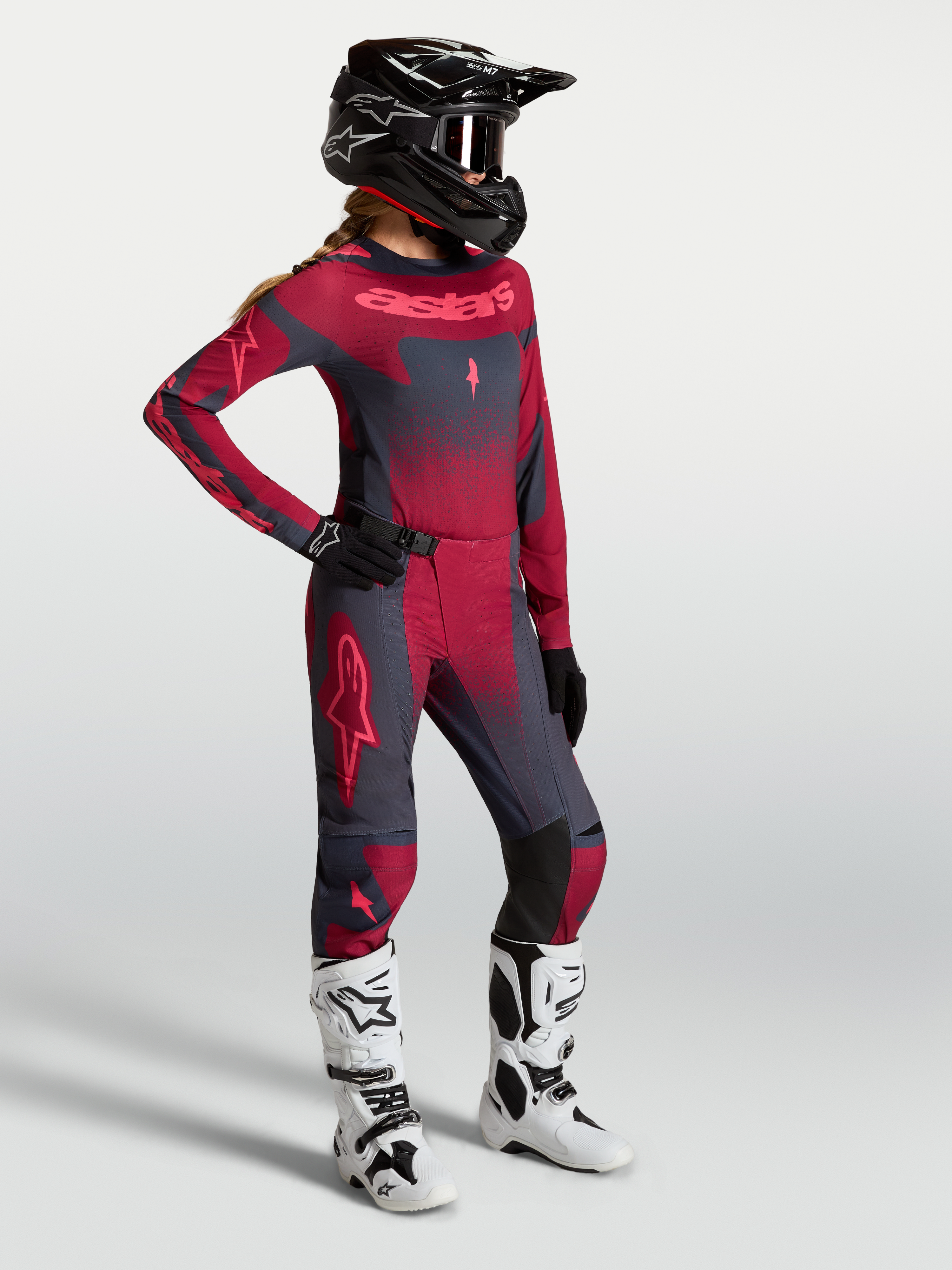 Alpinestars Stella Techstar Swan Gear Set e Pantaloni Stella Techstar Swan, completo da motocross per donna in rosso e grigio scuro, indossato con casco nero e stivali bianchi.