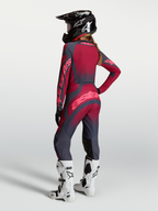 Alpinestars Maglia Stella Techstar Swan e Stella Techstar Swan Gear Set, completo da motocross per donna, rosso e grigio scuro, vista posteriore su modella con casco e stivali bianchi, abbigliamento tecnico off-road