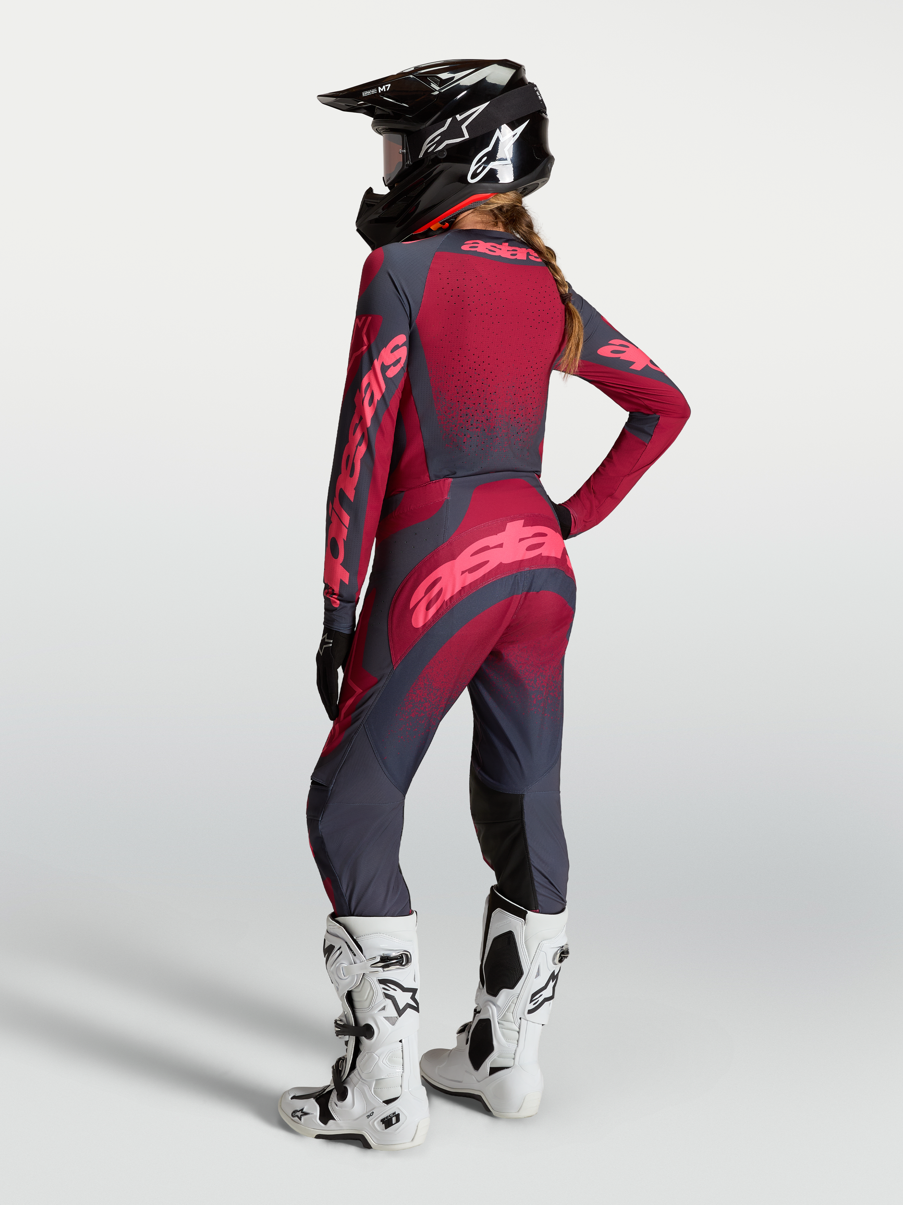 Alpinestars Maglia Stella Techstar Swan e Stella Techstar Swan Gear Set, completo da motocross per donna, rosso e grigio scuro, vista posteriore su modella con casco e stivali bianchi, abbigliamento tecnico off-road