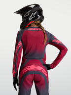 Alpinestars Maglia Stella Techstar Swan, maglia motocross da donna, cremisi e grigio scuro, tessuto elasticizzato traspirante con perforazioni laser, vista posteriore su modella con casco nero.