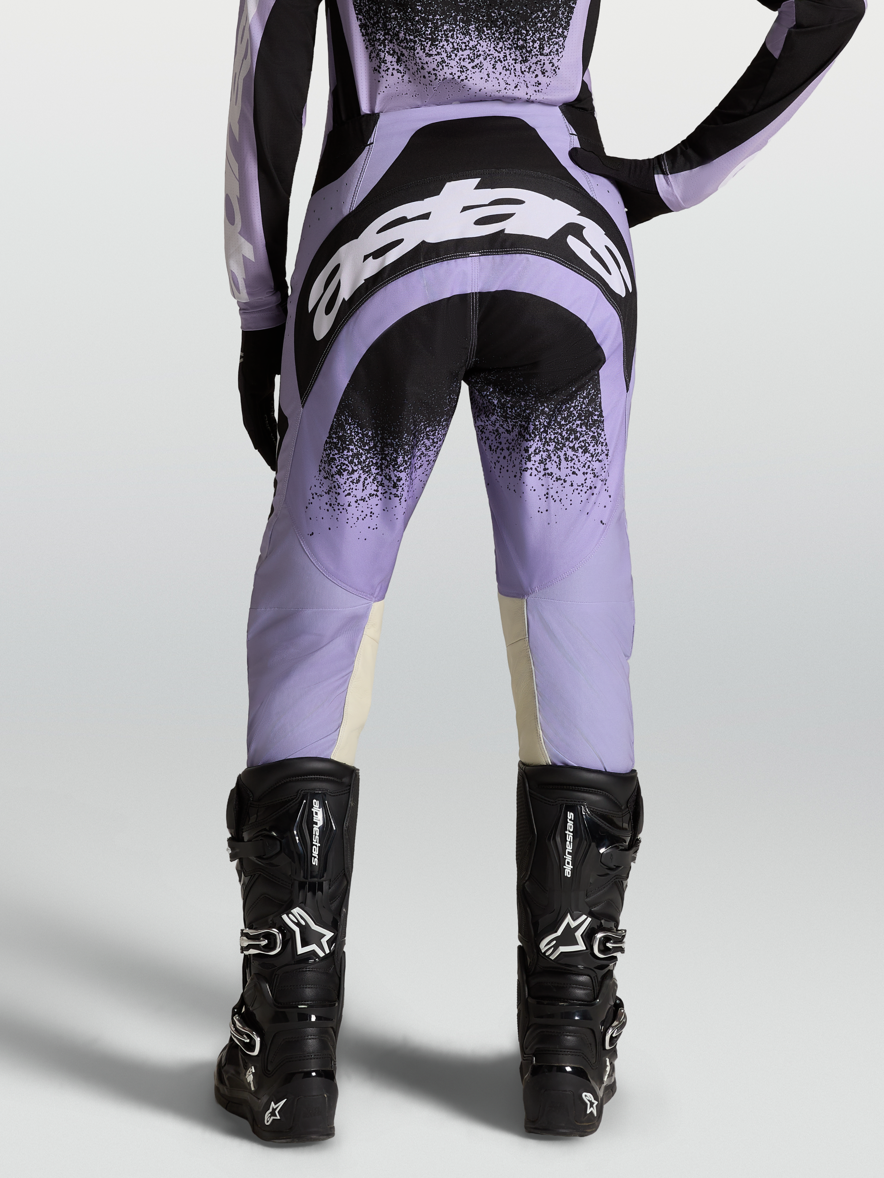 Alpinestars Pantaloni Stella Techstar Swan, pantaloni motocross da donna, viola e neri, indossati con stivali neri.