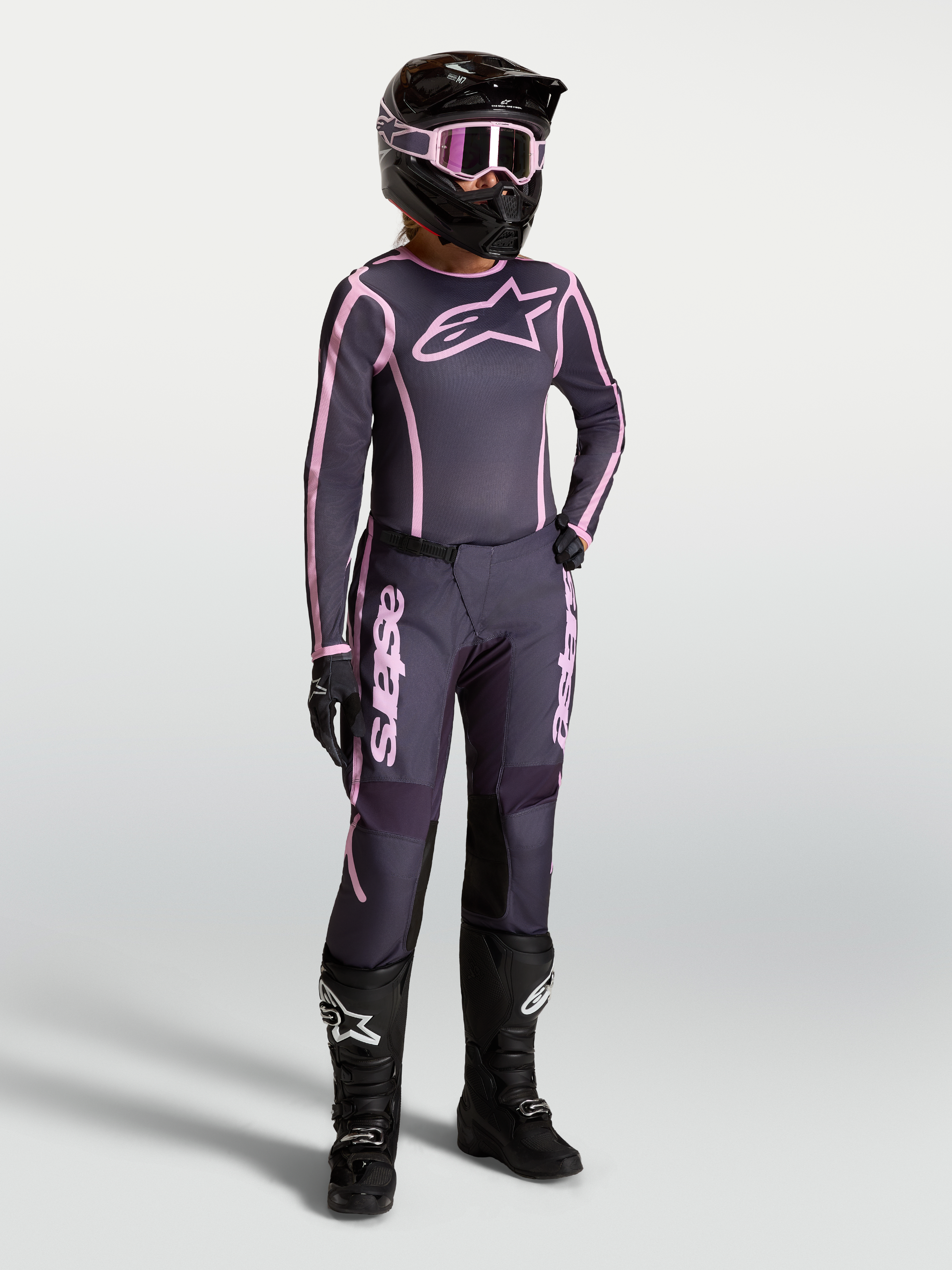 Maglia e completo Alpinestars Stella Fluid Apex V2, outfit da motocross da donna grigio e rosa con stivali da gara neri.