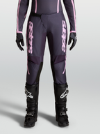 Alpinestars Pantaloni Stella Fluid Apex V2, pantaloni motocross da donna, grigio e rosa, chiusura a cricchetto e design precurvato, indossati con stivali neri per fuoristrada.