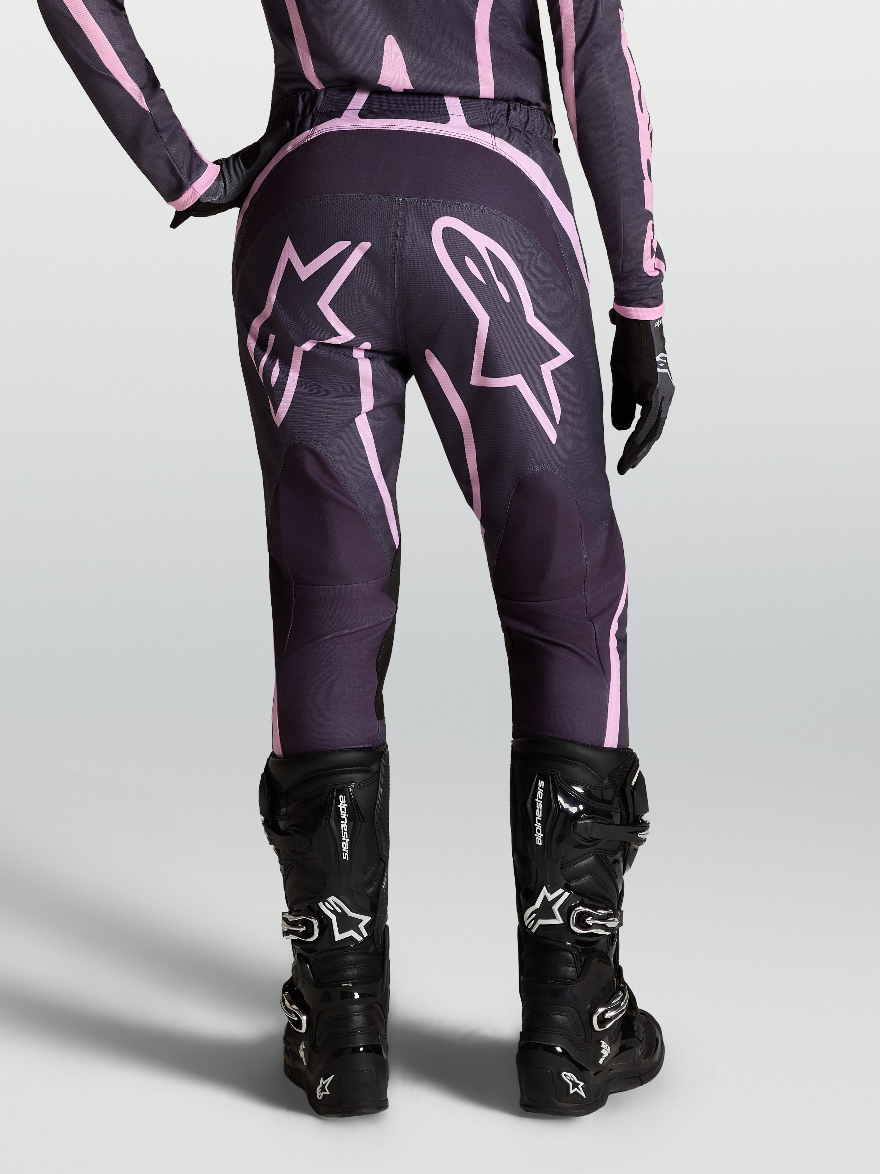 Alpinestars Pantaloni Stella Fluid Apex V2, pantaloni motocross da donna, grigio e rosa, con grafiche a stella e stivali moto neri.