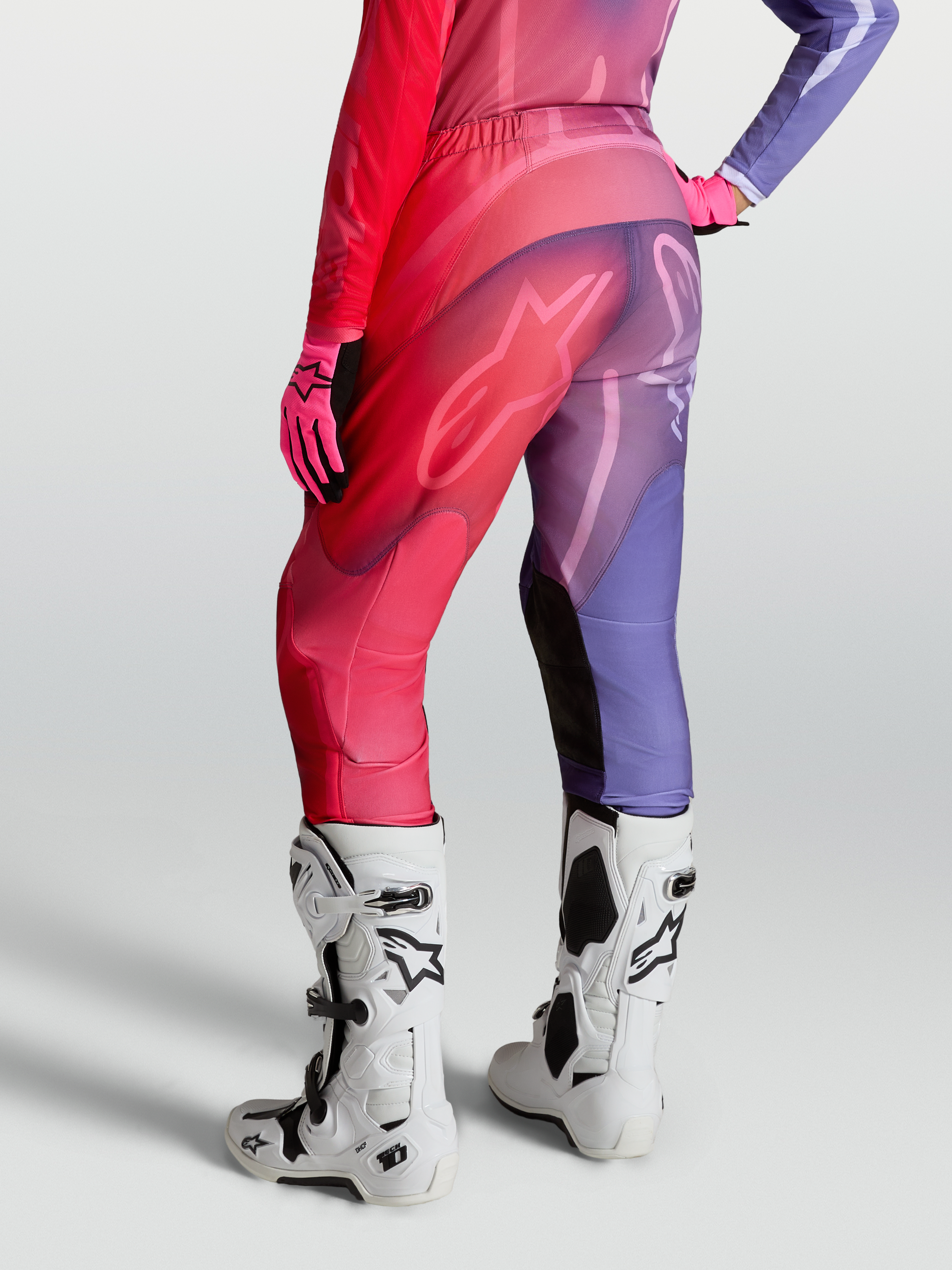 Alpinestars Pantaloni Stella Fluid Kepler, pantaloni motocross da donna, viola e rosso, gambe precurvate, pannelli stretch, indossati con stivali bianchi.