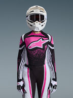 Alpinestars 2026 Stella Techstar Nomur Gear Set, completo da motocross da donna, rosa, nero e bianco con grande logo a stella, con maglia, pantaloni e guanti coordinati e un casco bianco, vista frontale su sfondo grigio
