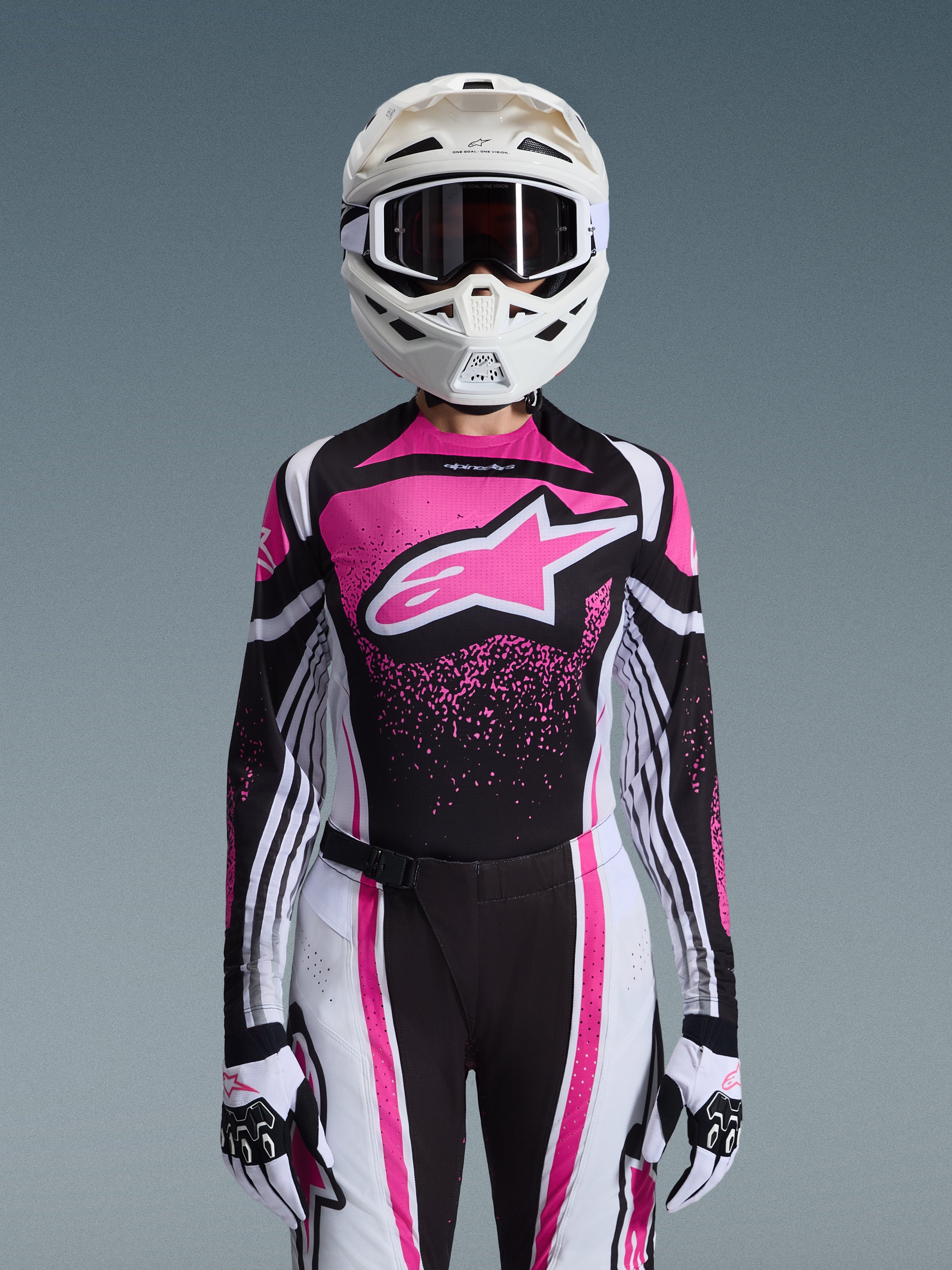 Alpinestars 2026 Stella Techstar Nomur Gear Set, completo da motocross da donna, rosa, nero e bianco con grande logo a stella, con maglia, pantaloni e guanti coordinati e un casco bianco, vista frontale su sfondo grigio