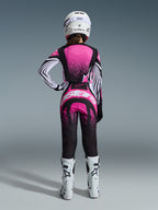 Alpinestars 2026 Stella Techstar Nomur Gear Set, pilota di motocross donna vista da dietro, maglia rosa e nera con maniche a righe bianche e motivo puntinato, pantaloni coordinati con logo Alpinestars bianco, casco bianco e stivali off-road bianchi