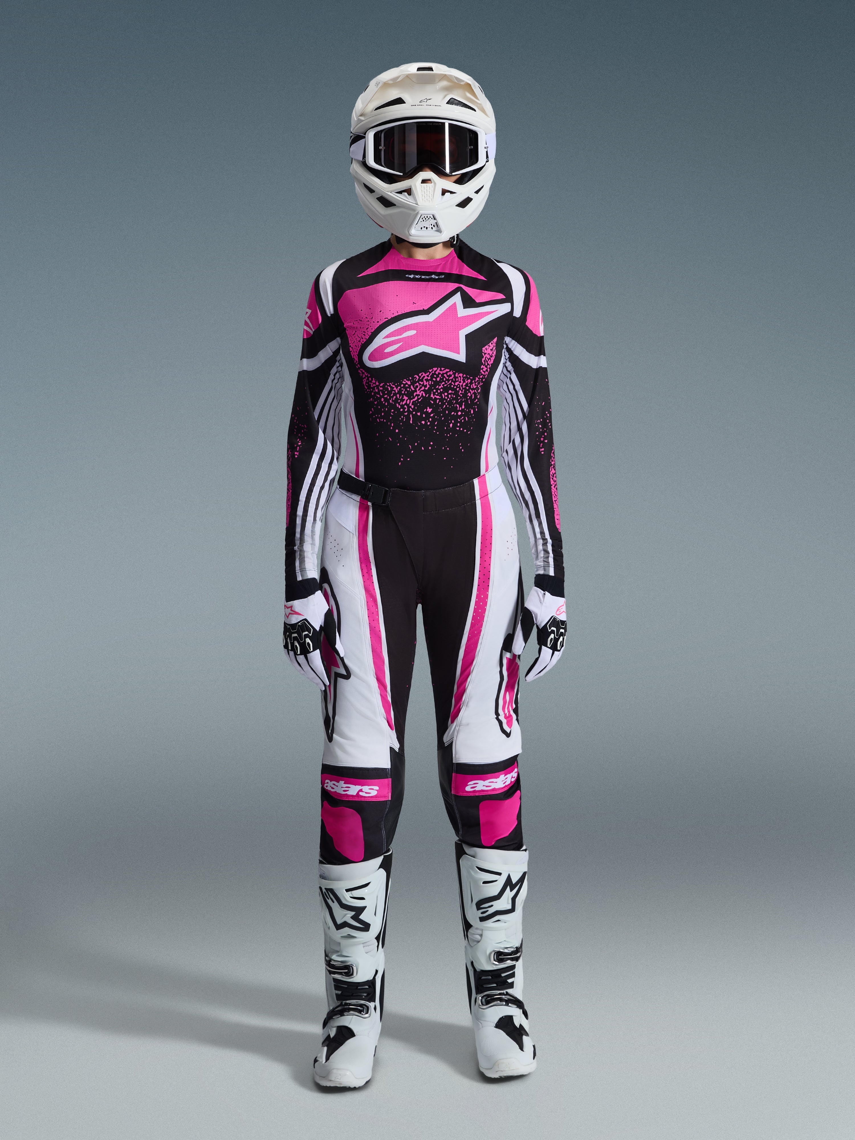 Alpinestars 2026 Woman Stella Techstar Nomur Gear Set, completo da motocross racing in nero, bianco e fucsia, maglia con grande logo a stella e design con schizzi rosa, pantaloni coordinati, casco bianco con maschera, stivali neri e bianchi, abbigliamento fuoristrada da donna coordinato