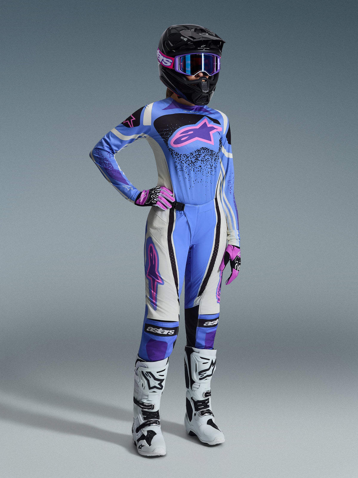 Set completo motocross Alpinestars Stella Techstar Nomur 2026, abbigliamento da donna con maglia azzurra e logo Astar rosa, pantaloni coordinati con pannelli bianchi e neri, casco nero con occhiali rosa e viola, guanti rosa e stivali da motocross bianchi