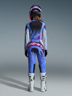 Vista posteriore di una pilota di motocross che indossa il completo Alpinestars Stella Techstar Nomur 2026, maglia e pantaloni blu con accenti rosa e bianchi, vistoso marchio rosa sul retro dei pantaloni, abbinati a stivali da motocross bianchi e un casco coordinato nero e rosa.