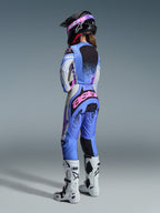 Alpinestars Stella Techstar Nomur Gear Set 2026, vista posteriore di una pilota di motocross con maglia e pantaloni in azzurro, bianco e rosa con dettagli punteggiati neri, casco nero e stivali bianchi, abbigliamento professionale da gara per donna.