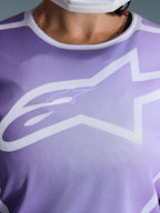 Alpinestars Stella Fluid Apex Jersey 2026, primo piano del petto, viola con grafiche bianche, caratterizzata da un grande logo Astars bianco su struttura in poli-tessuto mesh.