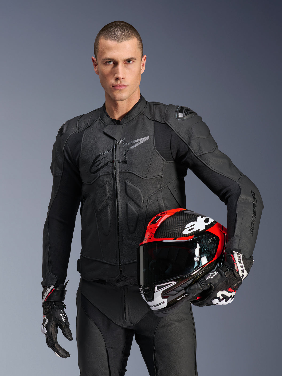 Alpinestars giacca in pelle Dusk, giacca da moto racing da uomo, nera, con protezioni Nucleon PLASMA, in pelle, certificata CE, indossata da un modello con casco rosso.
