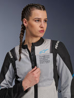 Donna che indossa la giacca Alpinestars Stella ST-2 Air in Ice Gray e Nero, ritratto in primo piano, con pannelli in rete per la ventilazione, marchio 'ALPINESTARS EXPLORATION EQUIPMENT' sul petto con logo blu, moderna giacca da moto adventure