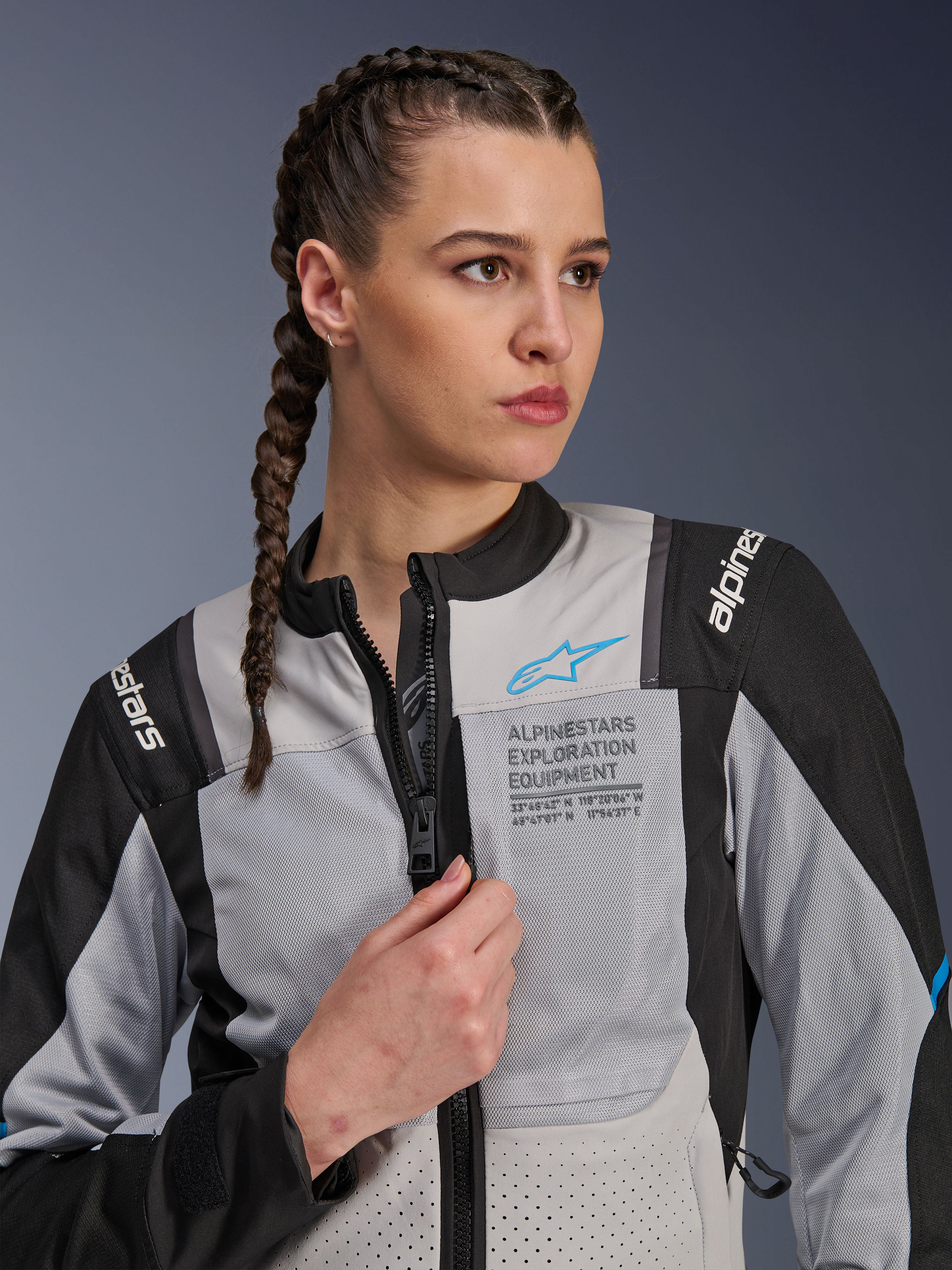 Donna che indossa la giacca Alpinestars Stella ST-2 Air in Ice Gray e Nero, ritratto in primo piano, con pannelli in rete per la ventilazione, marchio 'ALPINESTARS EXPLORATION EQUIPMENT' sul petto con logo blu, moderna giacca da moto adventure