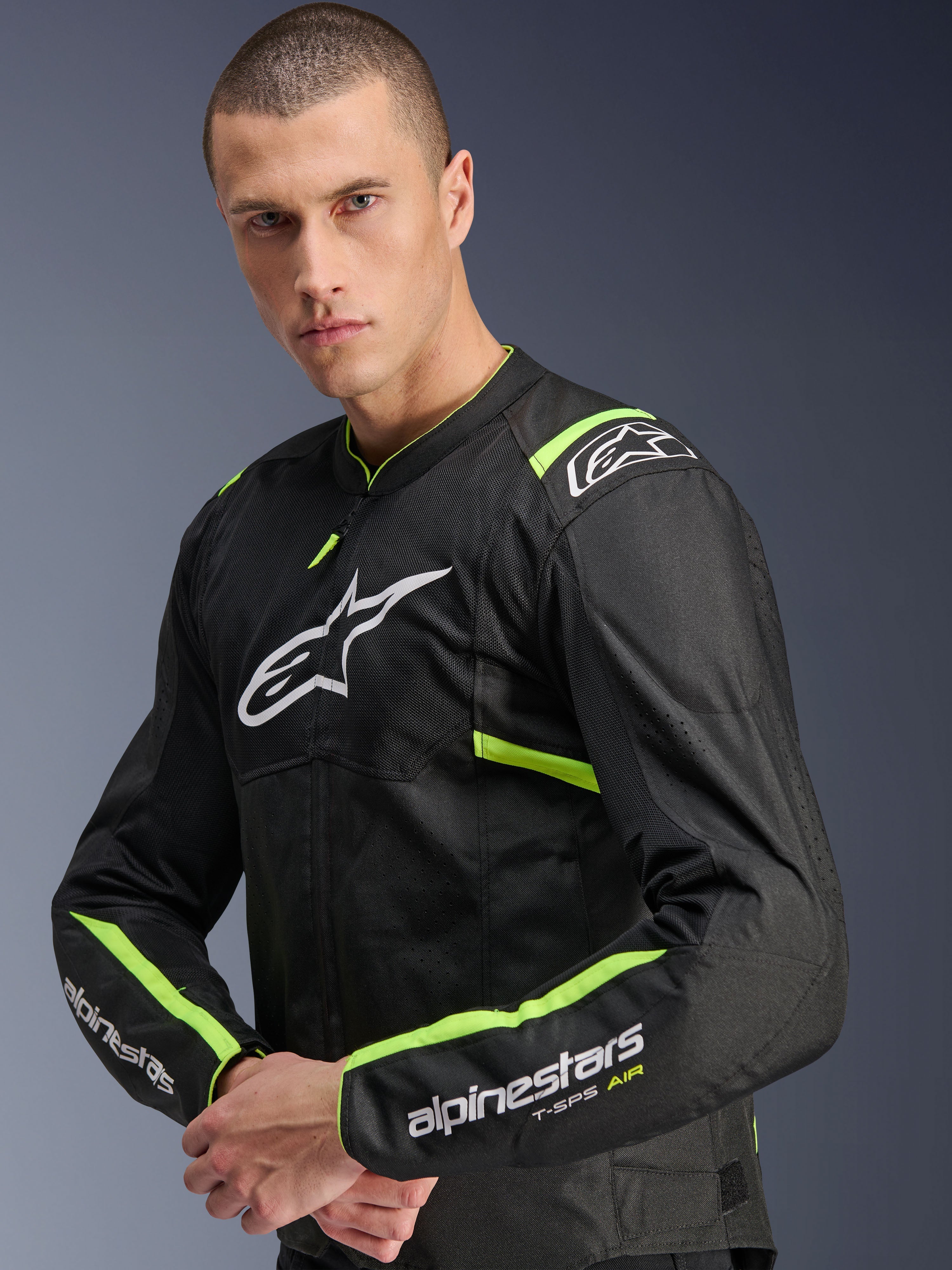 Giacca Alpinestars T-Sps Air V2, Nero Giallo Fluo, giacca da moto in tessuto indossata da un modello, dotata di pannelli in rete tecnica per il flusso d'aria, logo Alpinestars bianco sul petto e accenti giallo fluo su spalle e maniche.