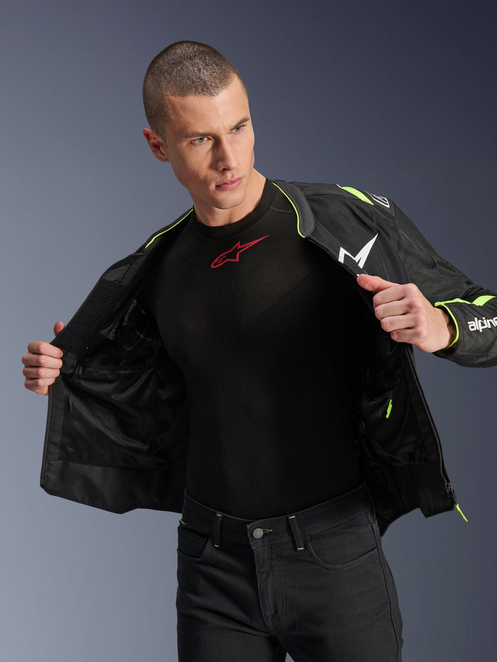 Modello che indossa la giacca Alpinestars T-Sps Air V2 in nero e giallo fluo, mostrata aperta per evidenziare la costruzione interna in rete e le tasche, abbinata a un base layer Alpinestars nero e pantaloni neri, stile abbigliamento da moto urbano