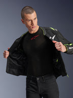 Modello che indossa la giacca Alpinestars T-Sps Air V2 in nero e giallo fluo, mostrata aperta per evidenziare la costruzione interna in rete e le tasche, abbinata a un base layer Alpinestars nero e pantaloni neri, stile abbigliamento da moto urbano