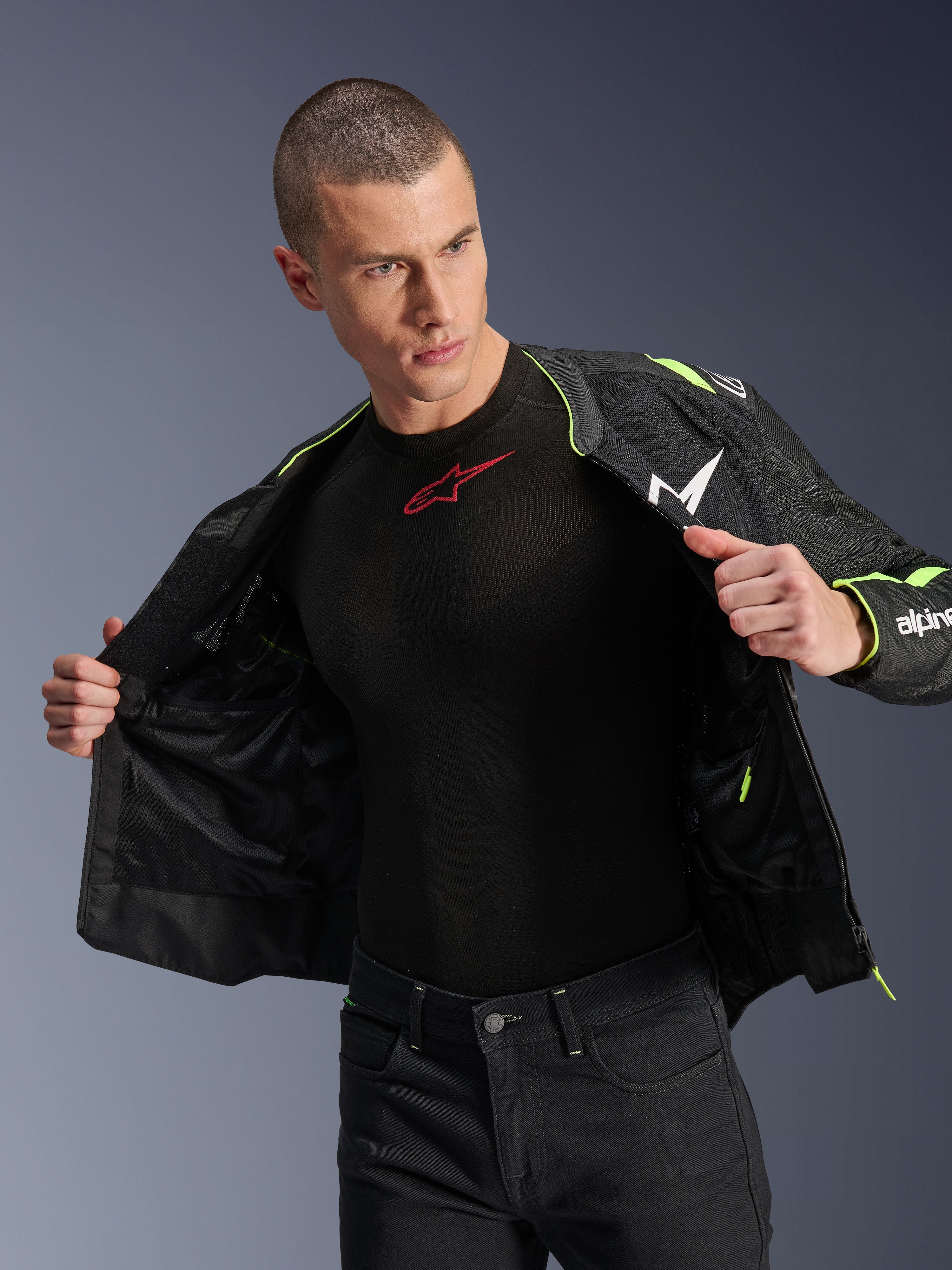 Modello che indossa la giacca Alpinestars T-Sps Air V2 in nero e giallo fluo, mostrata aperta per evidenziare la costruzione interna in rete e le tasche, abbinata a un base layer Alpinestars nero e pantaloni neri, stile abbigliamento da moto urbano