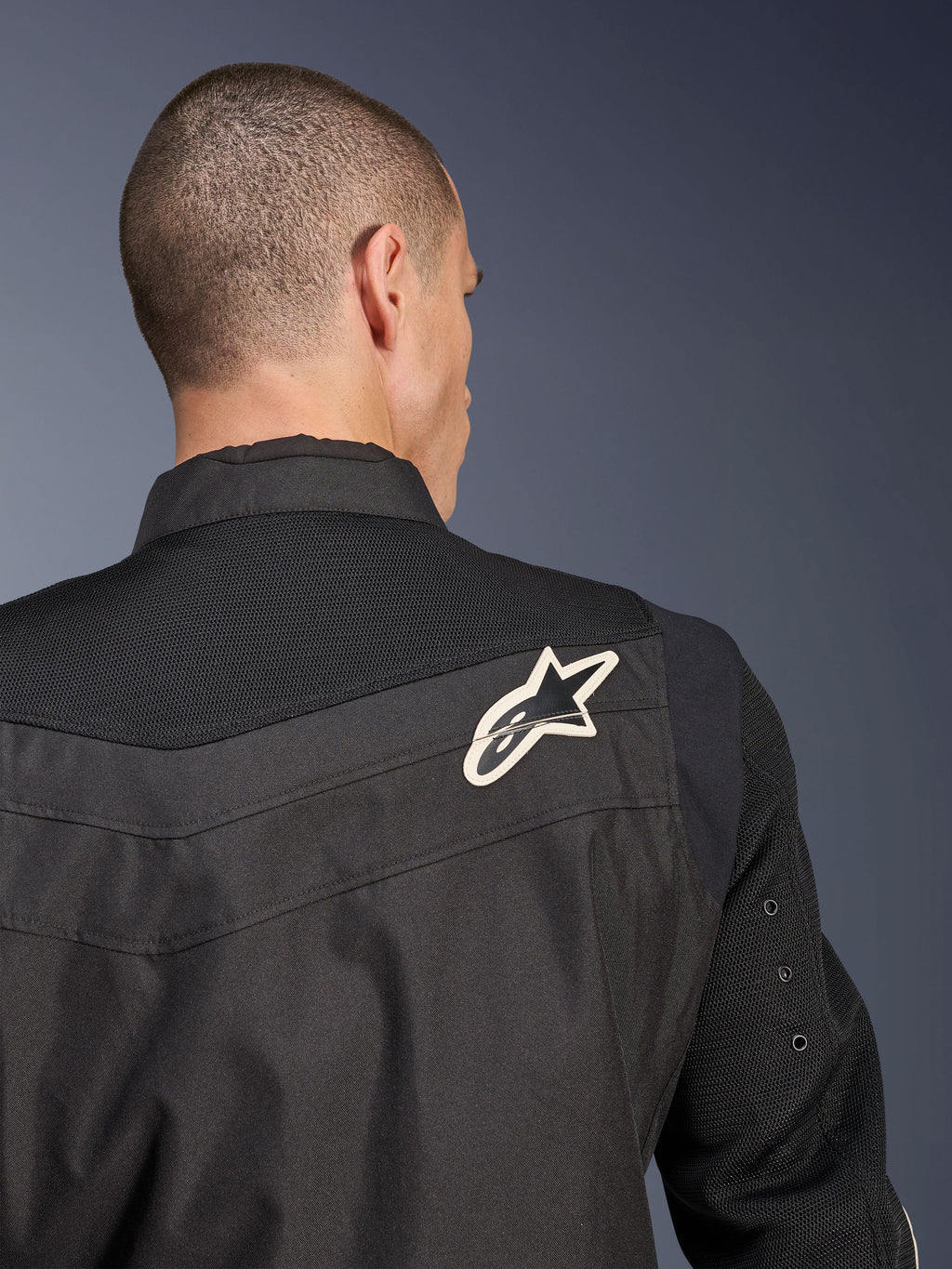 Giacca Alpinestars T-Dyno Air, giacca da moto in tessuto nero, vista ravvicinata posteriore che mette in risalto il giogo e le maniche in mesh 3D traspirante, con logo a stella bianco e nero sulla spalla destra.