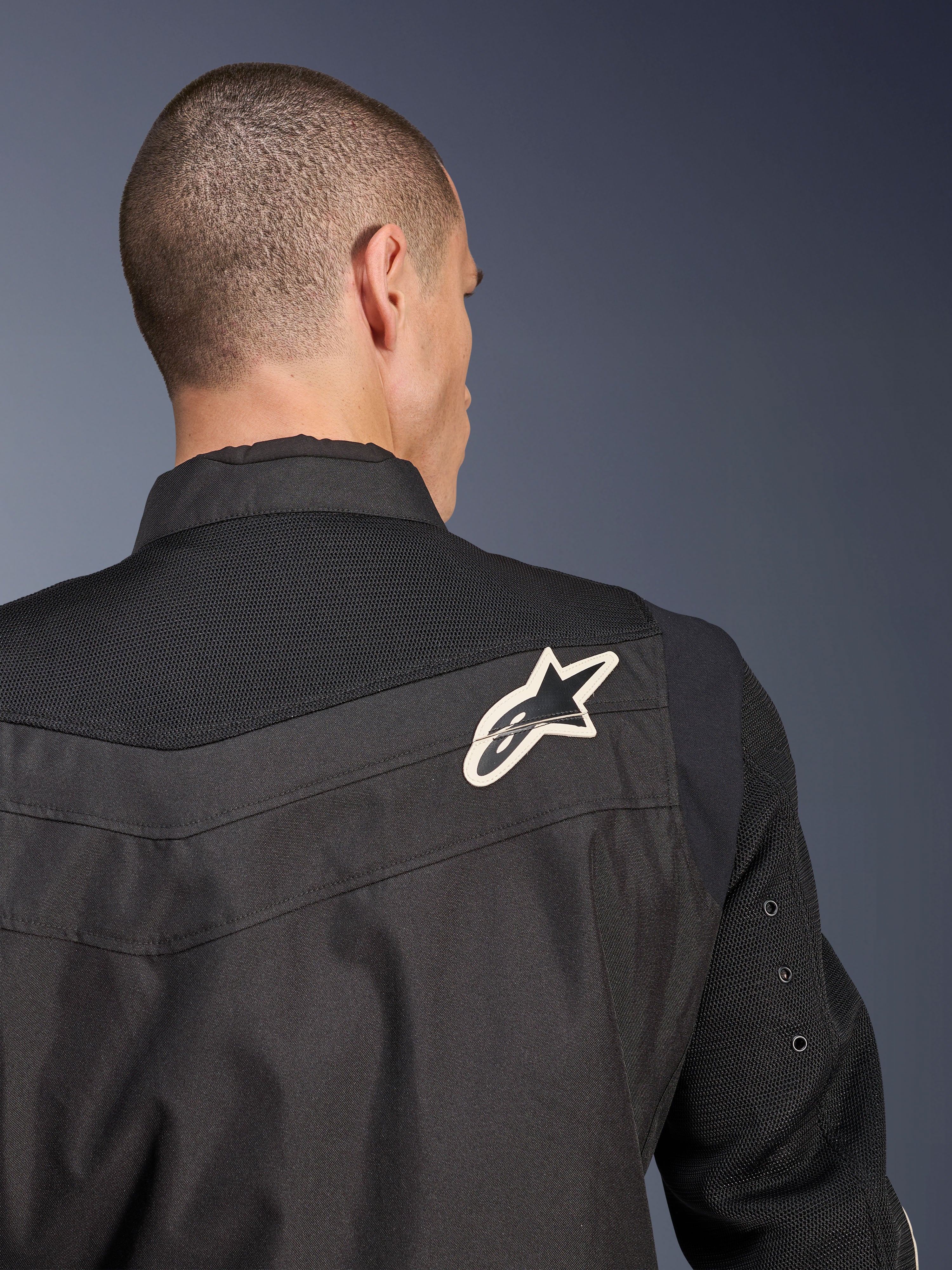 Giacca Alpinestars T-Dyno Air, giacca da moto in tessuto nero, vista ravvicinata posteriore che mette in risalto il giogo e le maniche in mesh 3D traspirante, con logo a stella bianco e nero sulla spalla destra.