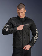 Alpinestars T-Dyno Air Jacket, nero, giacca da moto in tessuto con pannelli in rete 3D e loghi bianchi sulle maniche, indossata da un modello mentre chiude la zip frontale, stile urban street riding