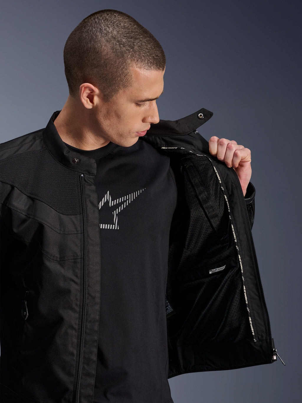 Giacca Alpinestars T-Dyno Air, nera, modello maschile che mostra la fodera interna in rete e l'etichetta dello scomparto impermeabile, indossata sopra una t-shirt nera con grafica, abbigliamento da moto urbano moderno