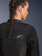 Alpinestars Stella T-Dyno Air Jacket, giacca da moto da donna nera, vista posteriore ravvicinata con pannelli in rete 3D sullo sprone e sulla parte superiore della schiena per la ventilazione, piccolo logo a stella bianco, indossata da una modella con capelli intrecciati.