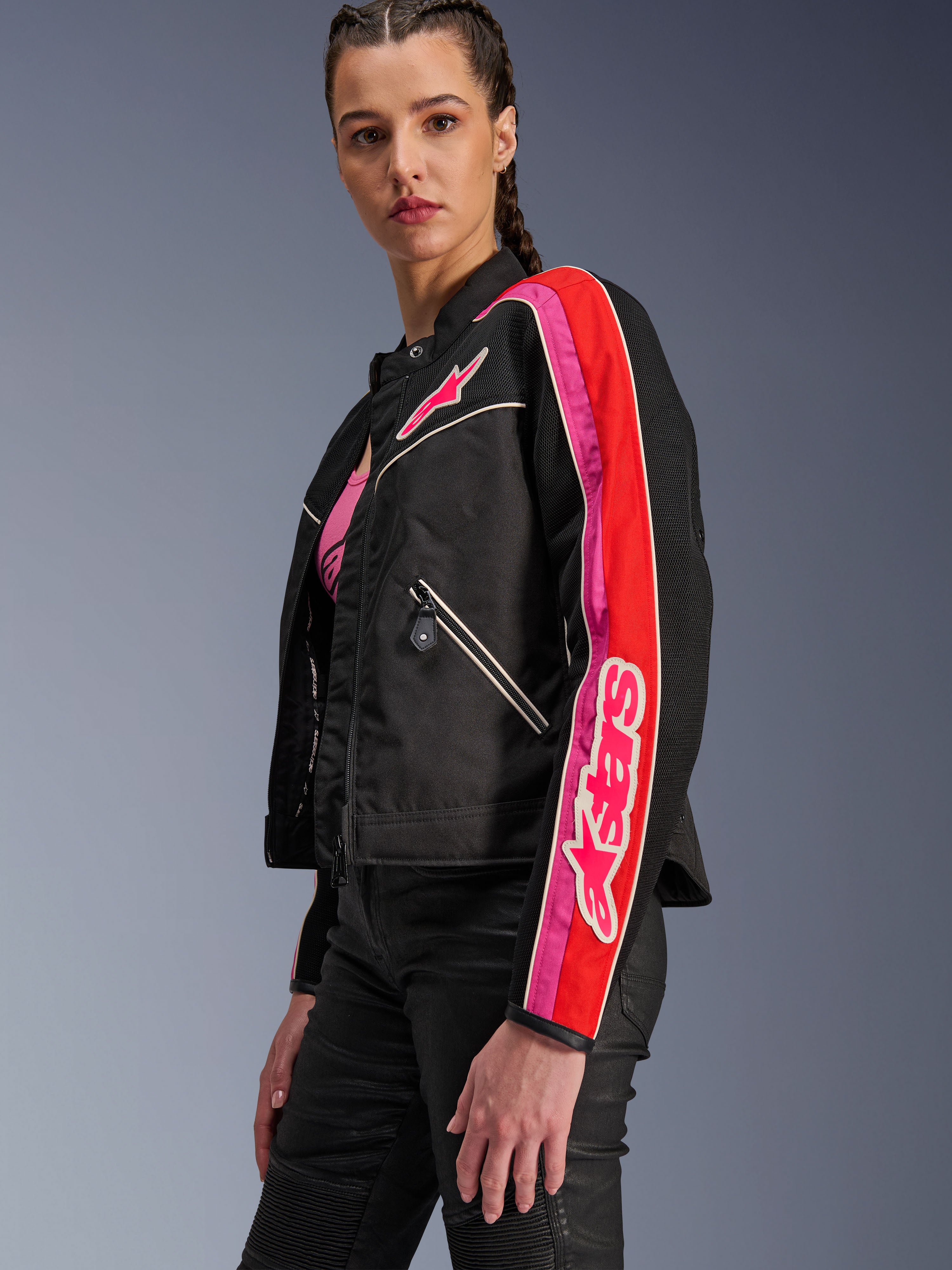 Alpinestars Stella T-Dyno Air Jacket, giacca da moto da donna, nero con accenti rosso brillante e fucsia, indossata con pantaloni neri, logo Astars rosa sul petto e sulla manica, vestibilità biker su misura con pannelli in rete per la ventilazione.
