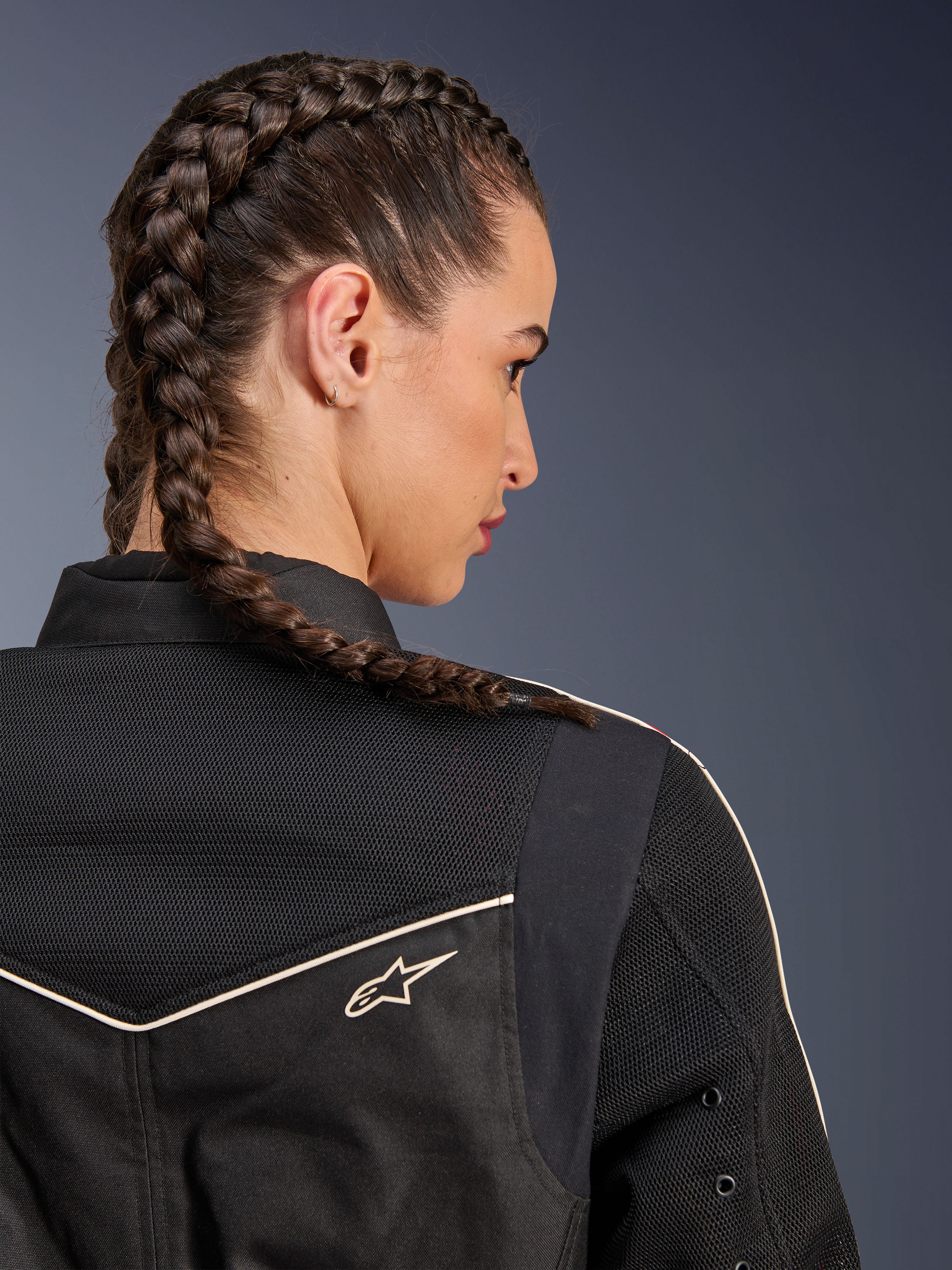 Donna che indossa la giacca Alpinestars Stella T-Dyno Air, vista posteriore ravvicinata focalizzata su spalle e giogo, nera con pannelli in rete 3D traspirante, profili bianchi e piccolo logo Astars, modella con capelli intrecciati, abbigliamento moto urban