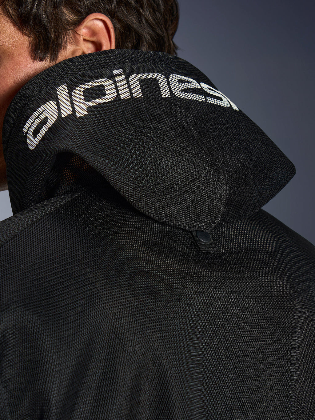 Alpinestars Chrome Superairflow Hoodie, nero, vista dettagliata del cappuccio in mesh 3D con marchio Alpinestars bianco sulla parte superiore, mostra il bottone di stabilizzazione posteriore, abbigliamento da moto in tessuto ventilato per calore estremo