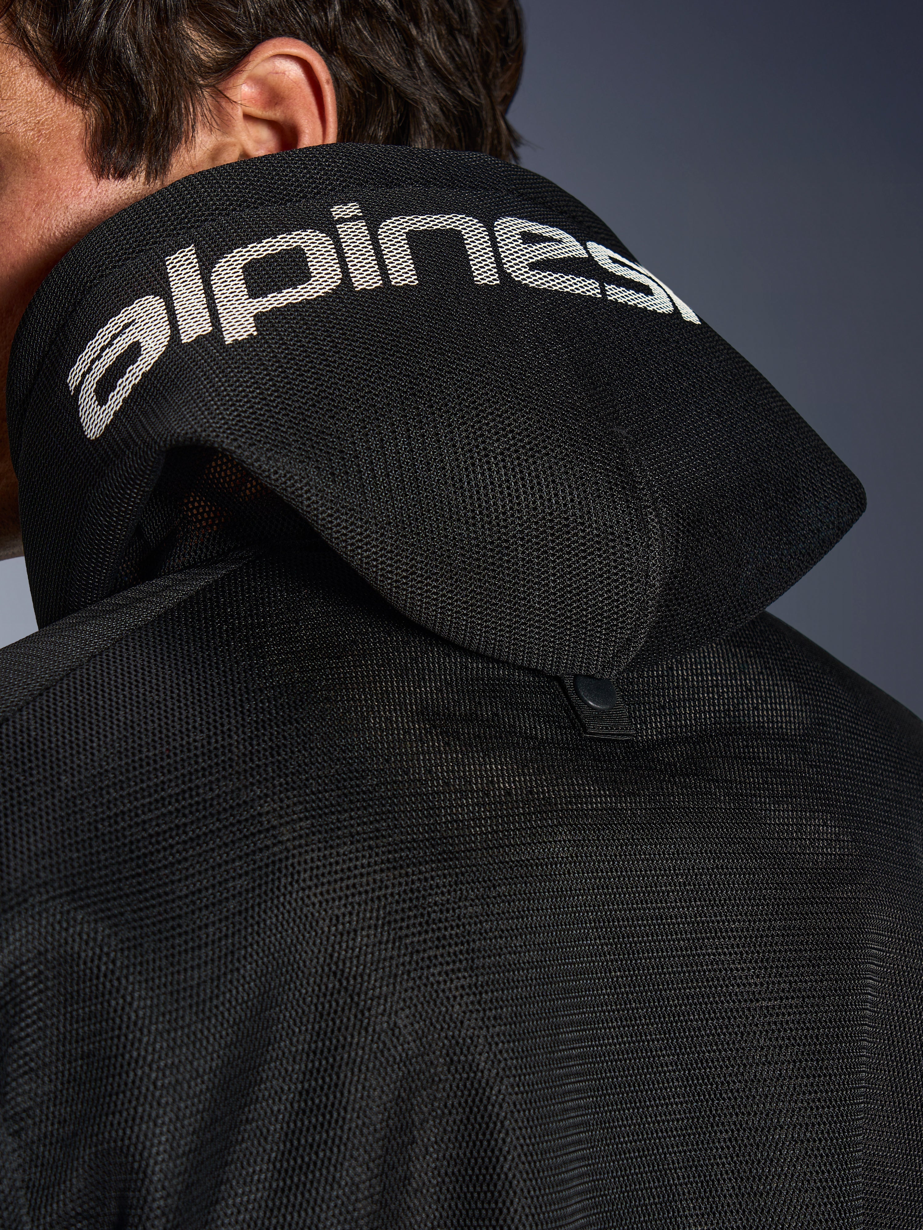 Alpinestars Chrome Superairflow Hoodie, nero, vista dettagliata del cappuccio in mesh 3D con marchio Alpinestars bianco sulla parte superiore, mostra il bottone di stabilizzazione posteriore, abbigliamento da moto in tessuto ventilato per calore estremo