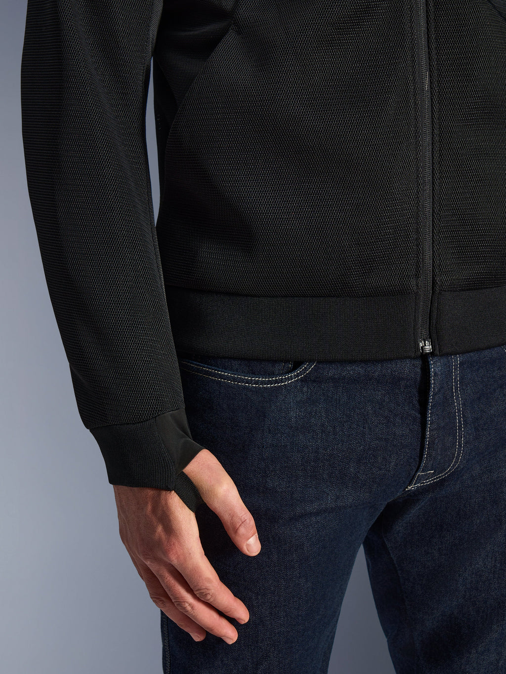 Alpinestars Chrome Superairflow Hoodie, nero, dettaglio del tessuto in mesh tecnico 3D ad alta resistenza, con polsino in maglia a coste elasticizzata e asola elastica per il pollice, indossata con jeans blu