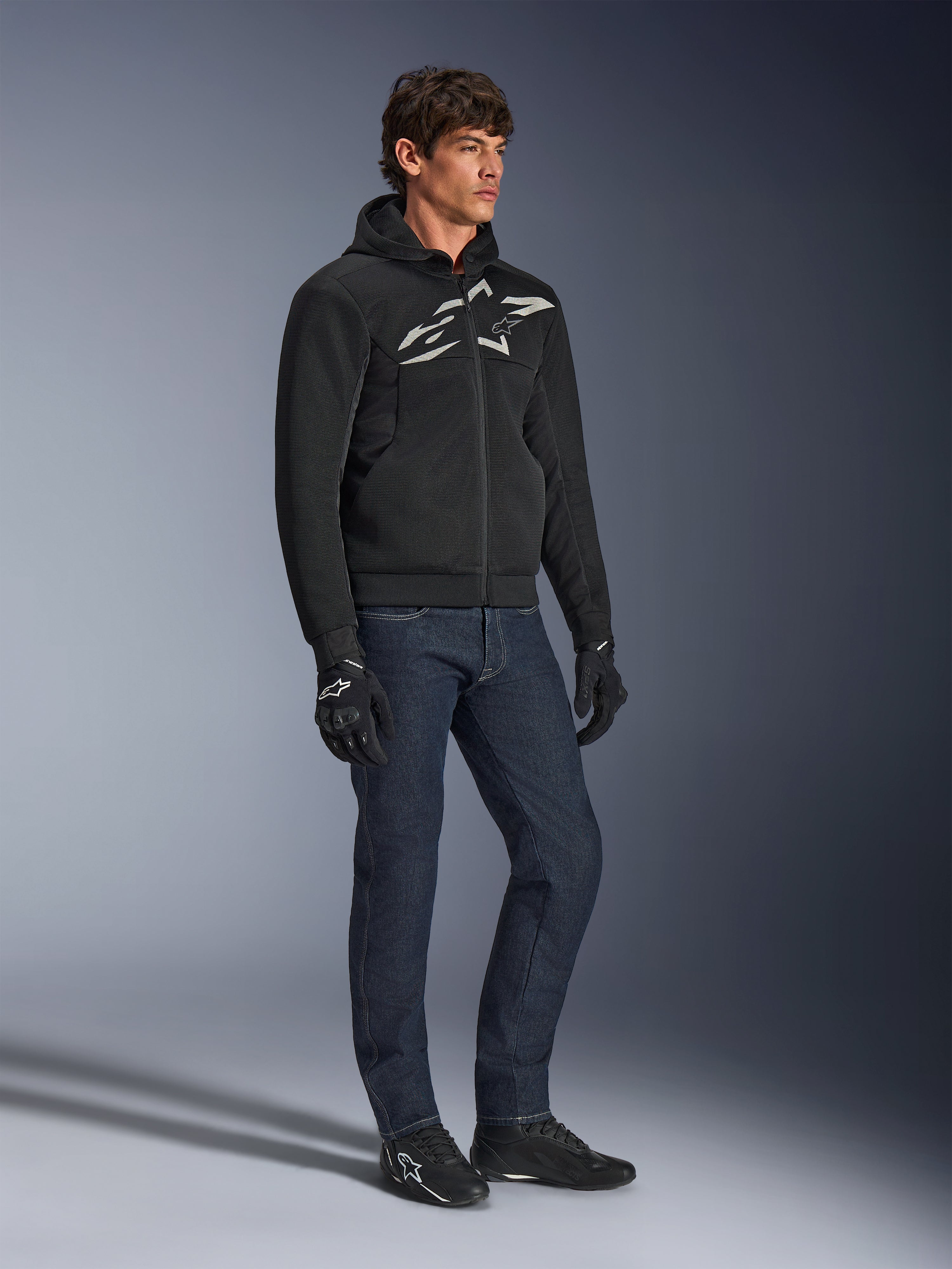 Felpa Alpinestars Chrome Superairflow, nera con logo bianco e grigio, costruzione in tessuto mesh 3D ventilato, indossata con jeans in denim blu scuro e guanti da moto neri, stile di guida urban sport.