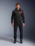 Alpinestars Chrome Air Sport Hoodie, nero e rosso fluo, giacca da moto urbana in pile tecnico, con grande logo Astars rosso sul petto e marchio sulla manica, indossata da un modello con pantaloni neri e scarpe da moto