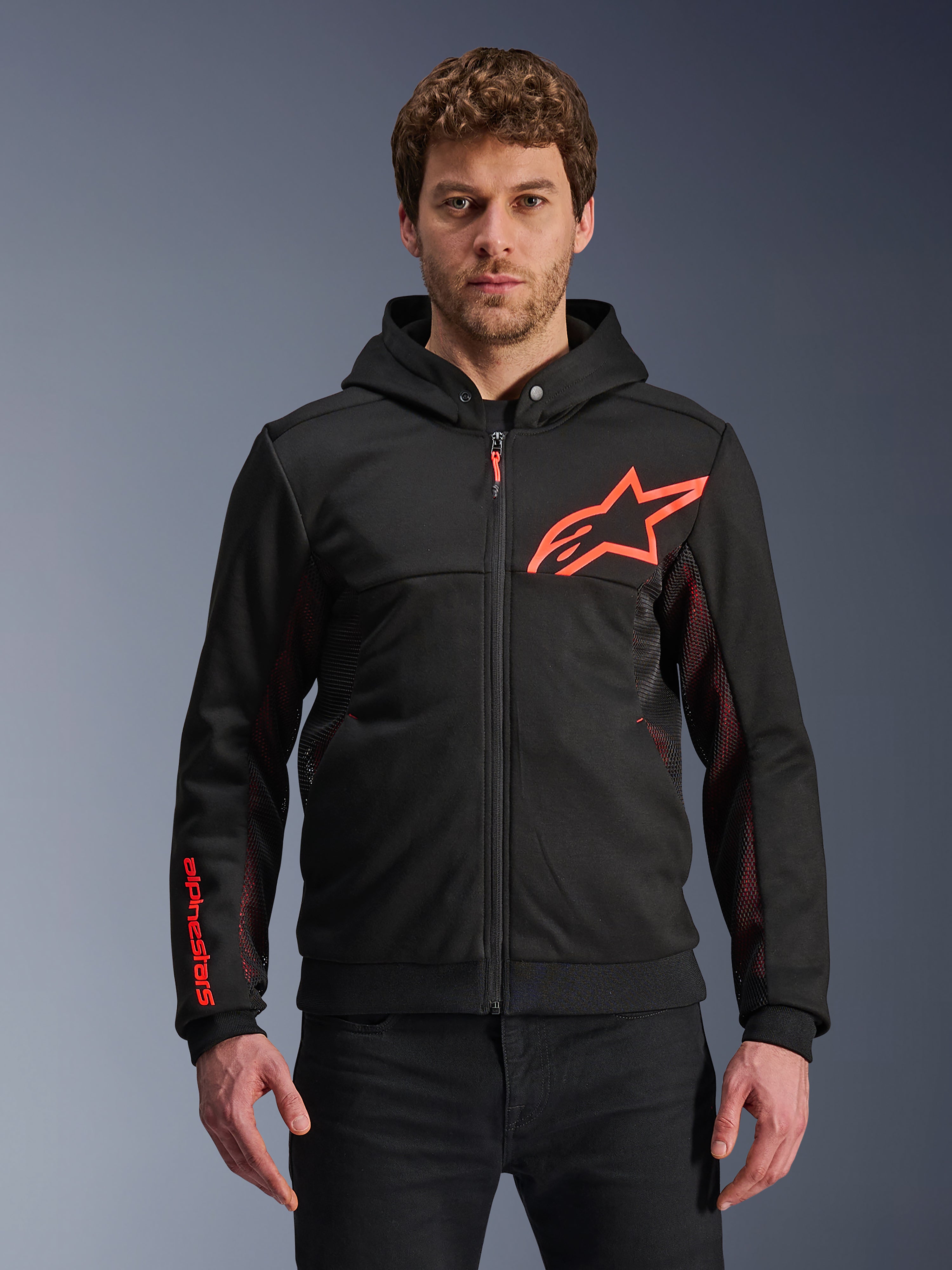 Alpinestars Chrome Air Sport Hoodie, felpa nera con cappuccio e zip, logo a stella rosso fluo e dettagli sulle maniche, pannelli laterali in mesh rosso per la ventilazione, abbigliamento urban riding casual indossato da un modello