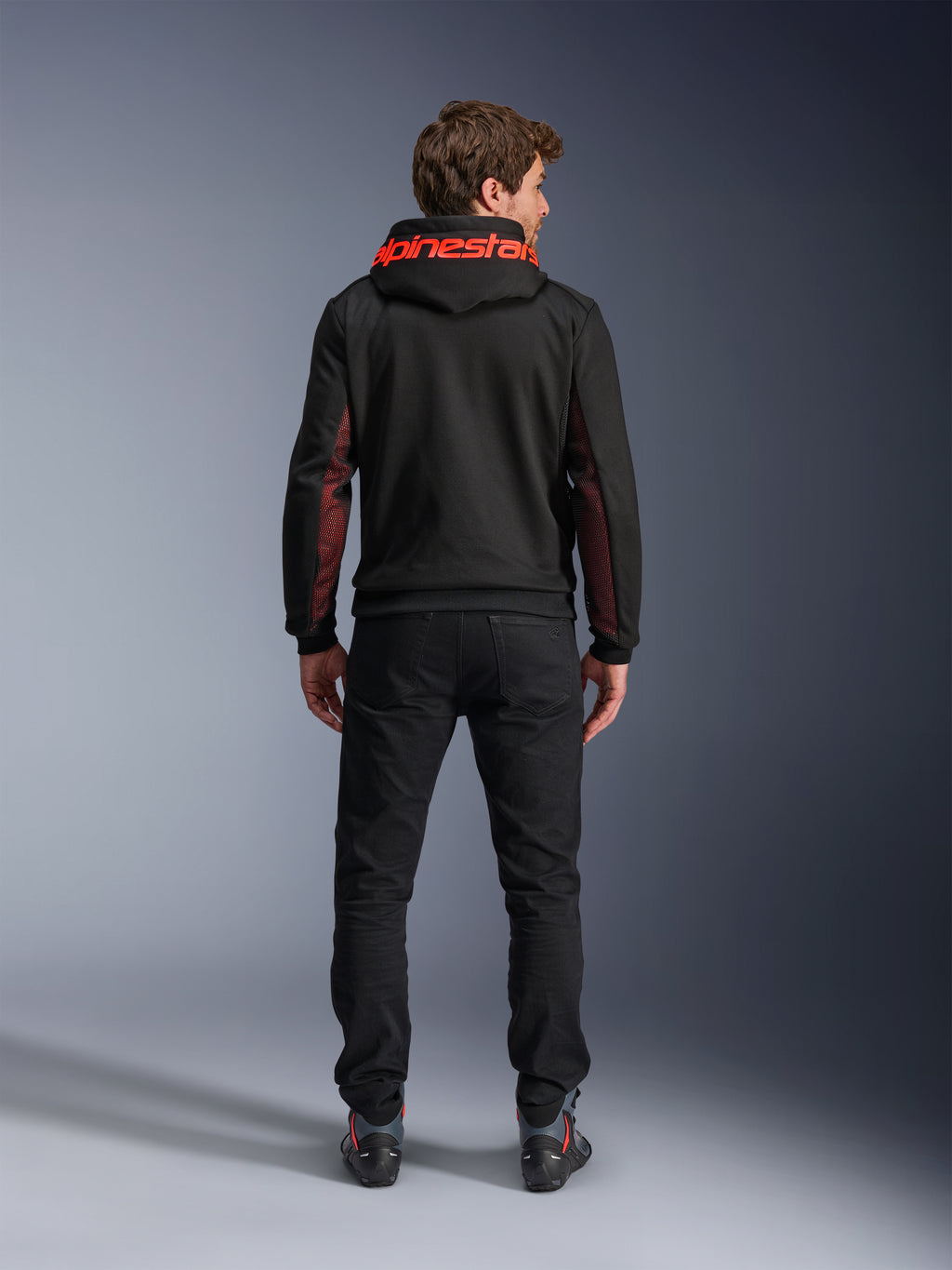 Alpinestars Chrome Air Sport Hoodie, nero e rosso fluo, vista posteriore di un uomo che indossa una giacca da moto casual, con logo Alpinestars rosso sul cappuccio e pannelli in mesh rossi sulle maniche, abbinata a pantaloni neri