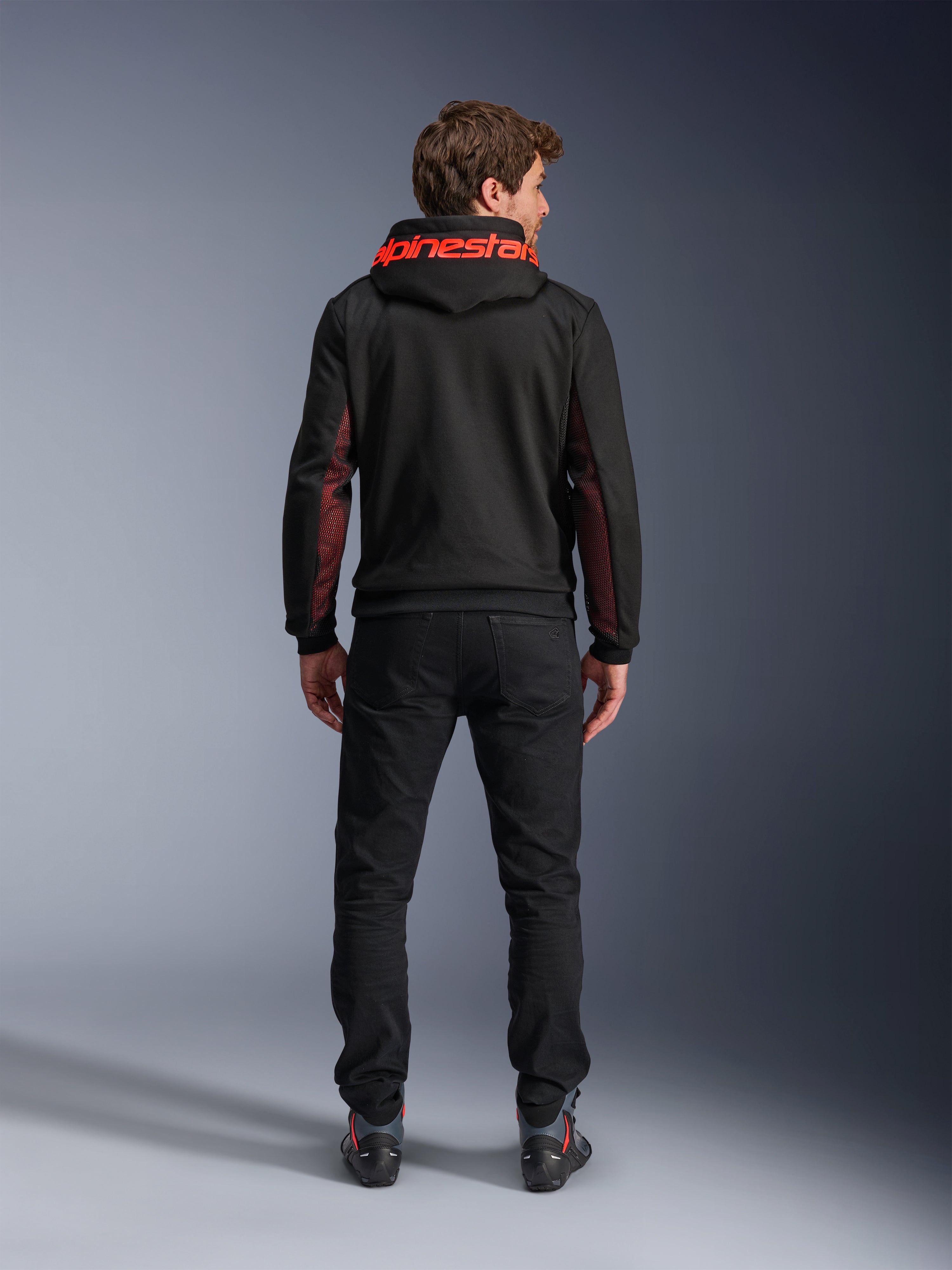 Alpinestars Chrome Air Sport Hoodie, nero e rosso fluo, vista posteriore di un uomo che indossa una giacca da moto casual, con logo Alpinestars rosso sul cappuccio e pannelli in mesh rossi sulle maniche, abbinata a pantaloni neri