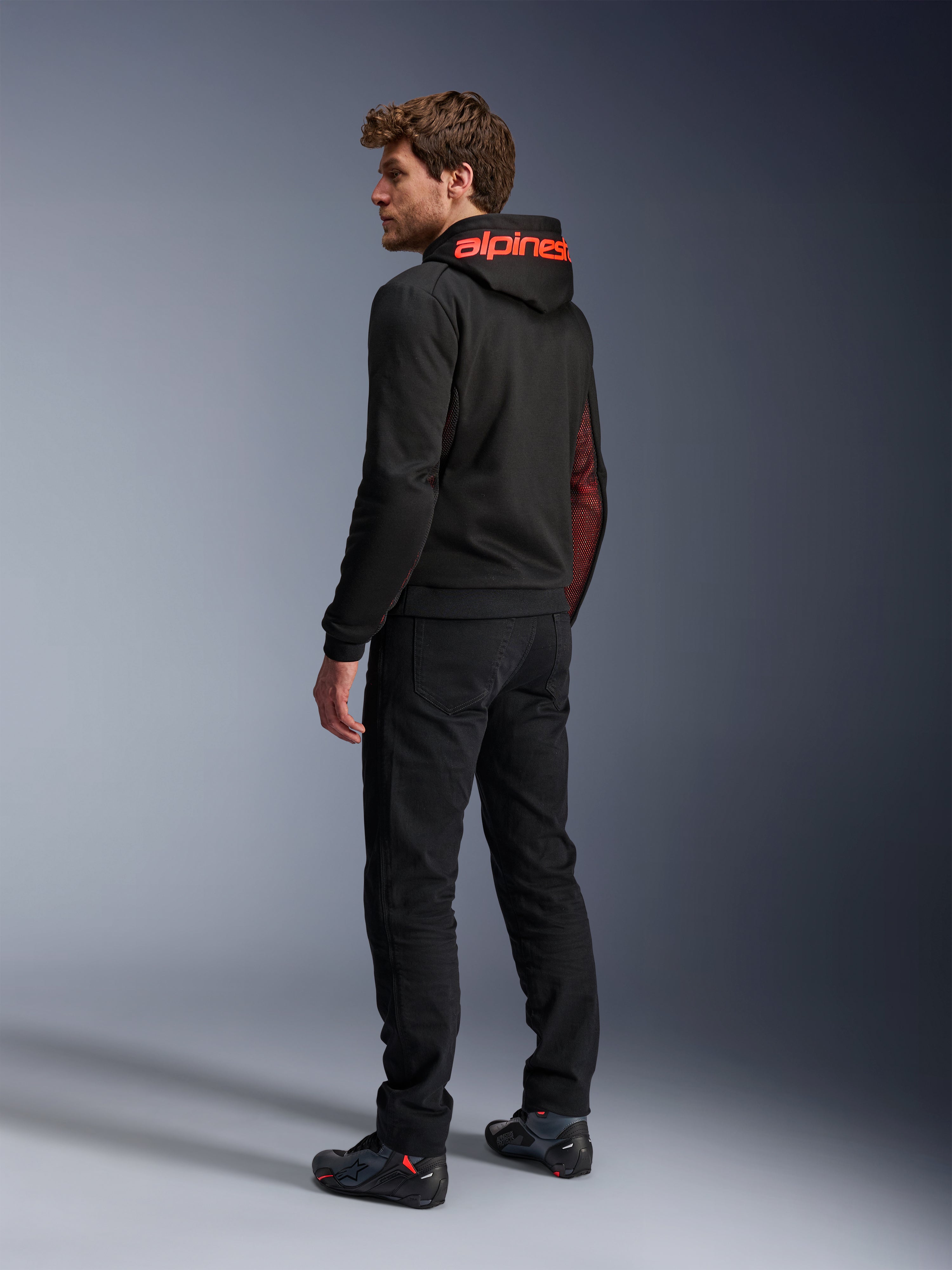 Alpinestars Chrome Air Sport Hoodie, felpa da moto urbana, Nero e Rosso Fluo, vista posteriore con marchio Alpinestars rosso sul cappuccio e pannelli laterali in mesh, indossata con pantaloni da guida neri e calzature tecniche