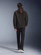 Alpinestars Radium Tech Hoodie, giacca da moto urbana, nera, vista posteriore con scritta 'ALPINE' in rosso acceso sul cappuccio, indossata con pantaloni neri e sneakers, guscio tecnico elegante per il pendolarismo.