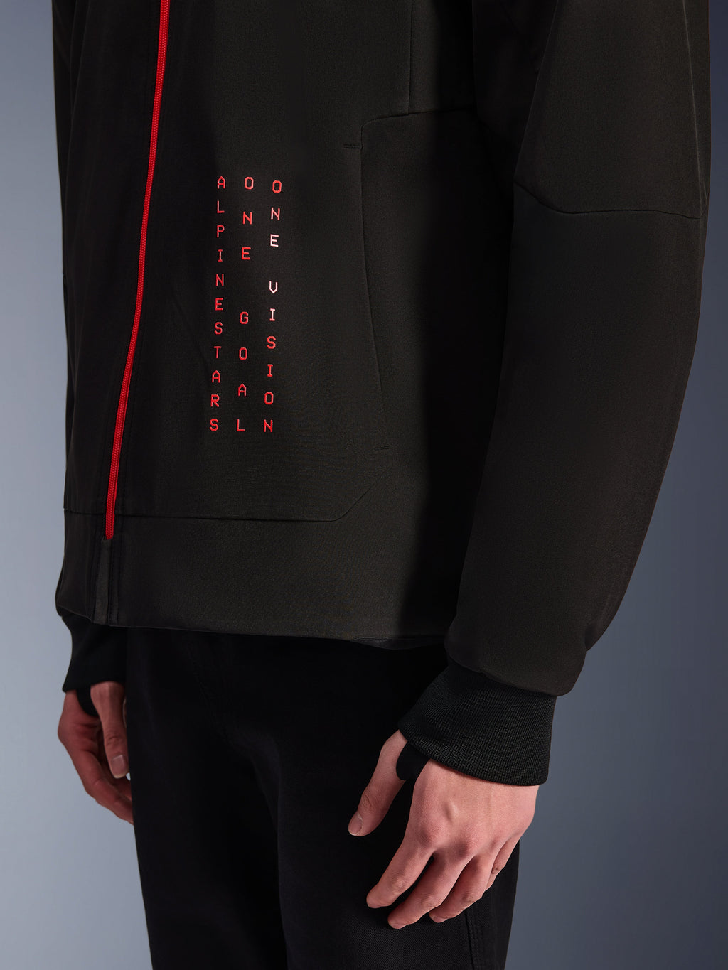 Alpinestars Radium Tech Hoodie, giacca da moto urban, nero e rosso acceso, primo piano della grafica frontale con testo verticale rosso "ALPINESTARS ONE GOAL ONE VISION", cerniera rossa e polsino a coste con foro per il pollice.
