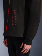Alpinestars Radium Tech Hoodie, giacca da moto urban, nero e rosso acceso, primo piano della grafica frontale con testo verticale rosso "ALPINESTARS ONE GOAL ONE VISION", cerniera rossa e polsino a coste con foro per il pollice.