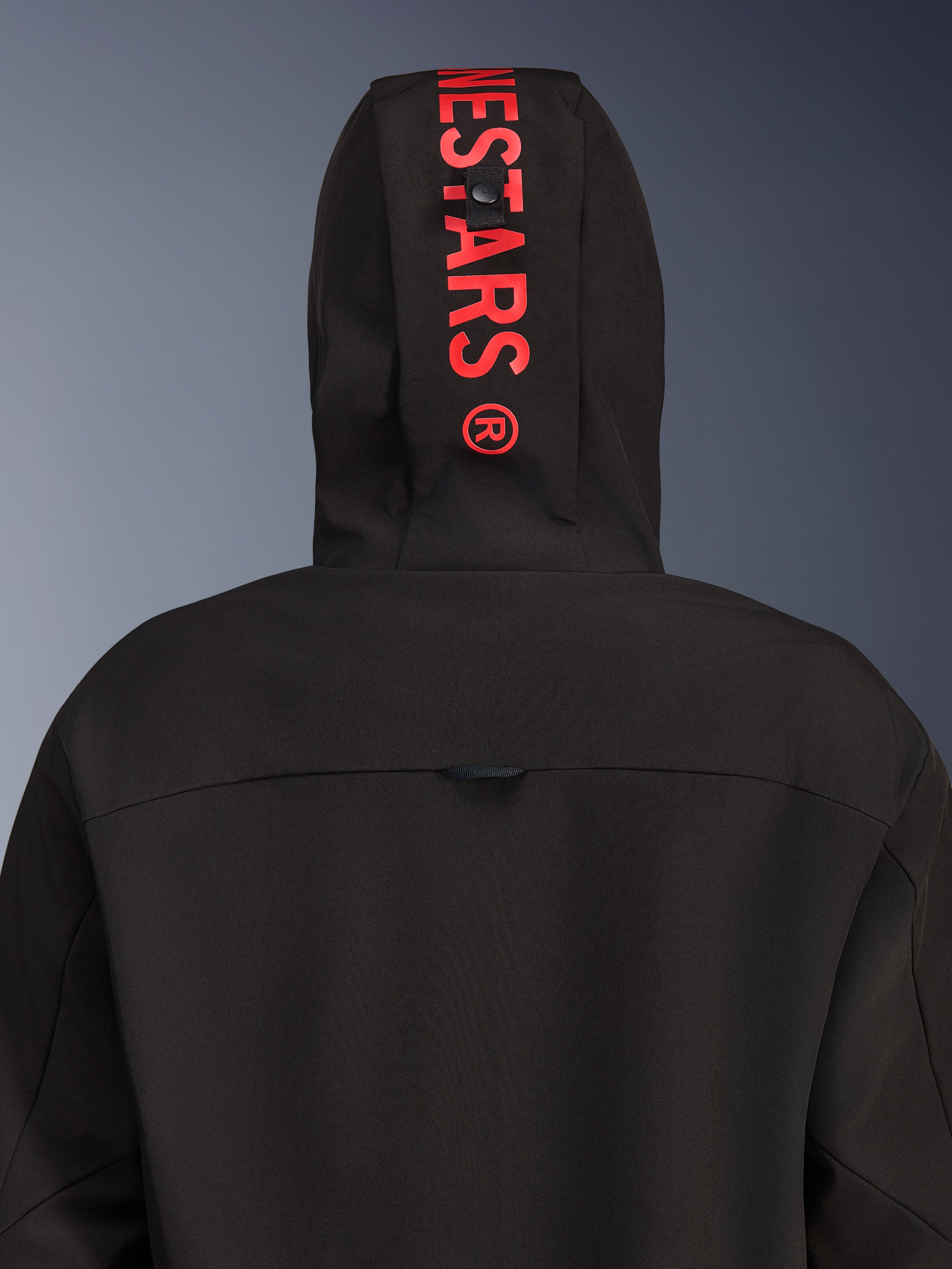 Alpinestars Radium Tech Hoodie, giacca da moto urbana, nero con rosso brillante, vista posteriore focalizzata sul cappuccio con logo verticale rosso, guscio in tessuto antivento e design contemporaneo.