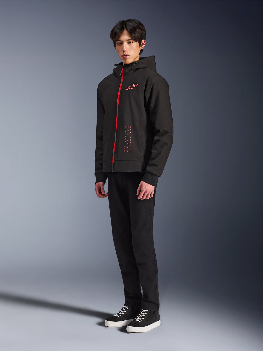 Alpinestars Radium Tech Hoodie, Nero Rosso Brillante, felpa tecnica per la guida urbana con cerniera frontale rossa e logo sul petto, indossata da un modello con pantaloni neri e sneakers nere con suola bianca, scatto in studio a figura intera