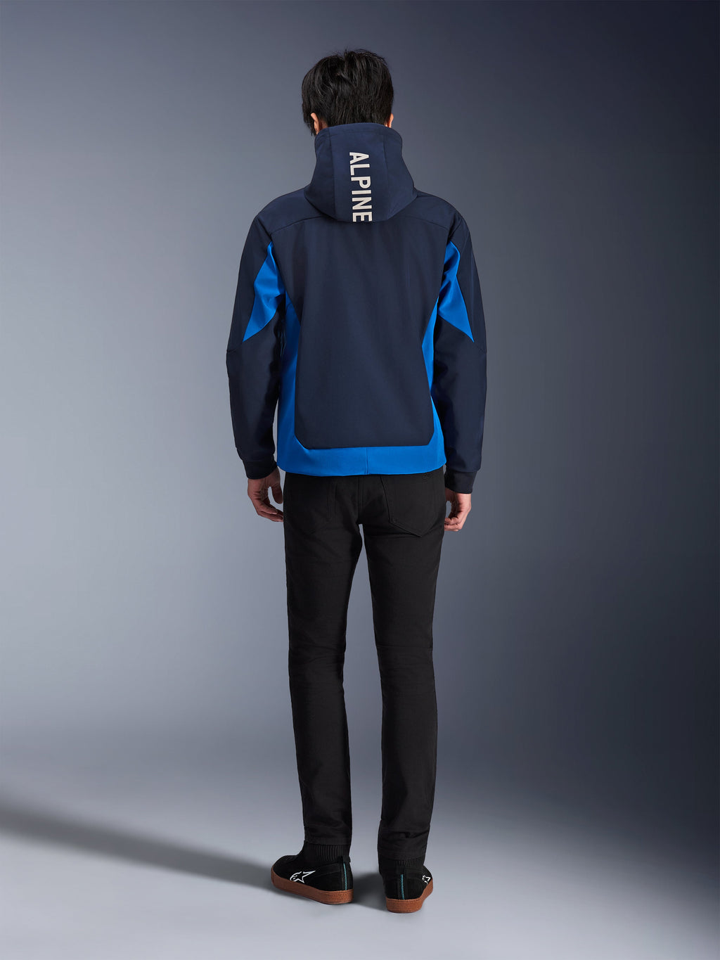Alpinestars Radium Tech Hoodie, Night Navy e Royal Blue, vista posteriore che mostra il branding verticale 'ALPINE' sul cappuccio, pannelli laterali e orlo blu royal, felpa da moto urbana casual con guscio 3L antivento, indossata con pantaloni neri