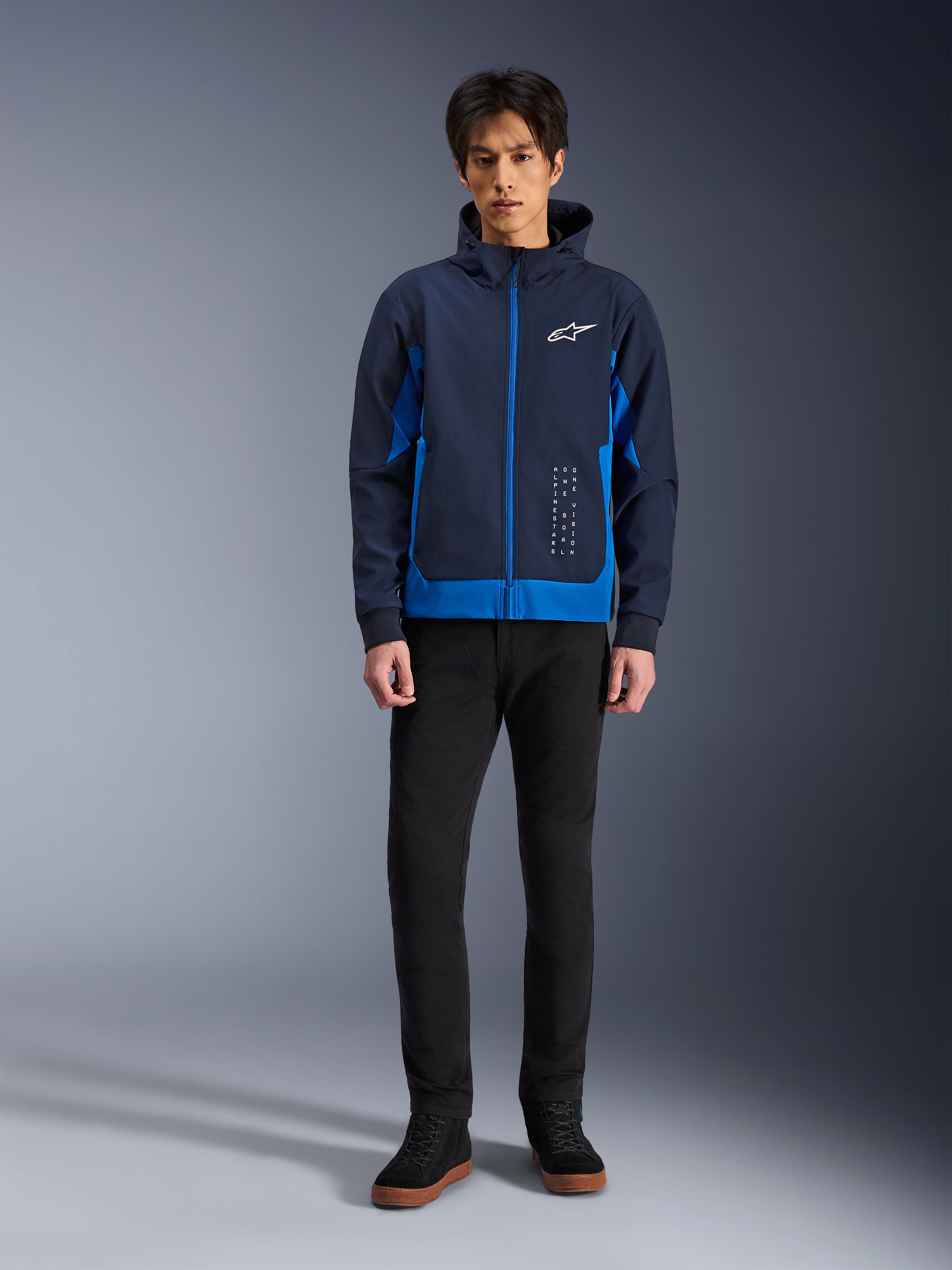 Alpinestars Radium Tech Hoodie, felpa da moto urbana in blu notte e blu reale, guscio tecnico antivento, design streetwear casual indossata con pantaloni neri e sneakers alte, con logo bianco sul petto